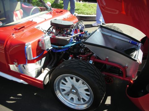 1998 Ford Crown Victoria - The exposed engine bay of a red custom car reveals a V8 engine with aftermarket modifications and polished components.