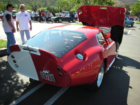 1998 Ford Crown Victoria - Red Shelby Cobra Daytona Coupe replica at a car show, hood and trunk open, with other cars and people in background.