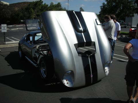 1998 Ford Crown Victoria - A silver sports car with dual black racing stripes is displayed with its hood open at a car show.