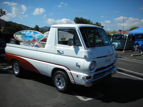 1998 Ford Crown Victoria - A vintage Dodge A100 pickup truck is parked at an outdoor event, carrying surfboards in its bed.