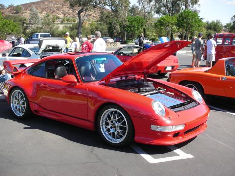 1998 Ford Crown Victoria - A red Porsche 911 with its hood open at a car show, with other vehicles and attendees around.
