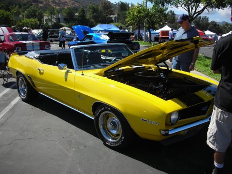1998 Ford Crown Victoria - A bright yellow 1969 Camaro convertible is displayed with its hood open at a car show, revealing the engine and a '350' badge on the fender.