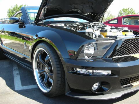 1998 Ford Crown Victoria - A black convertible sports car is parked with its hood open, revealing the engine compartment. A red car is parked behind it.