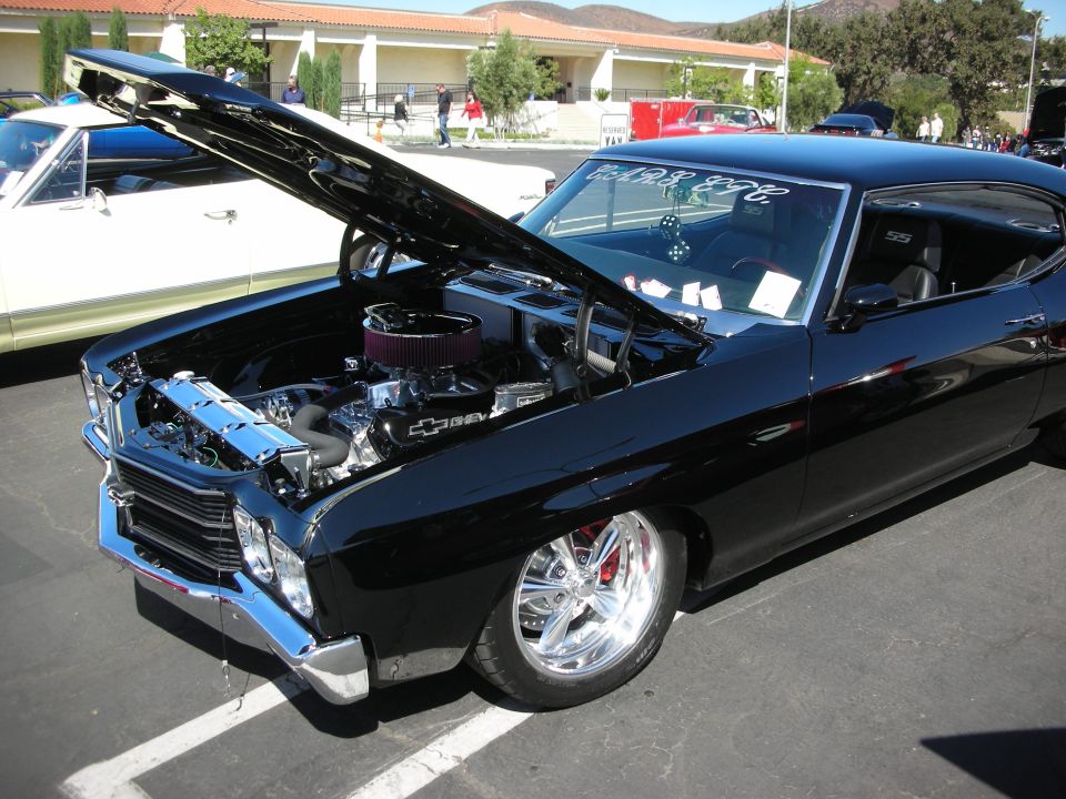 Black classic car with hood open showing engine. Another car is parked next to it