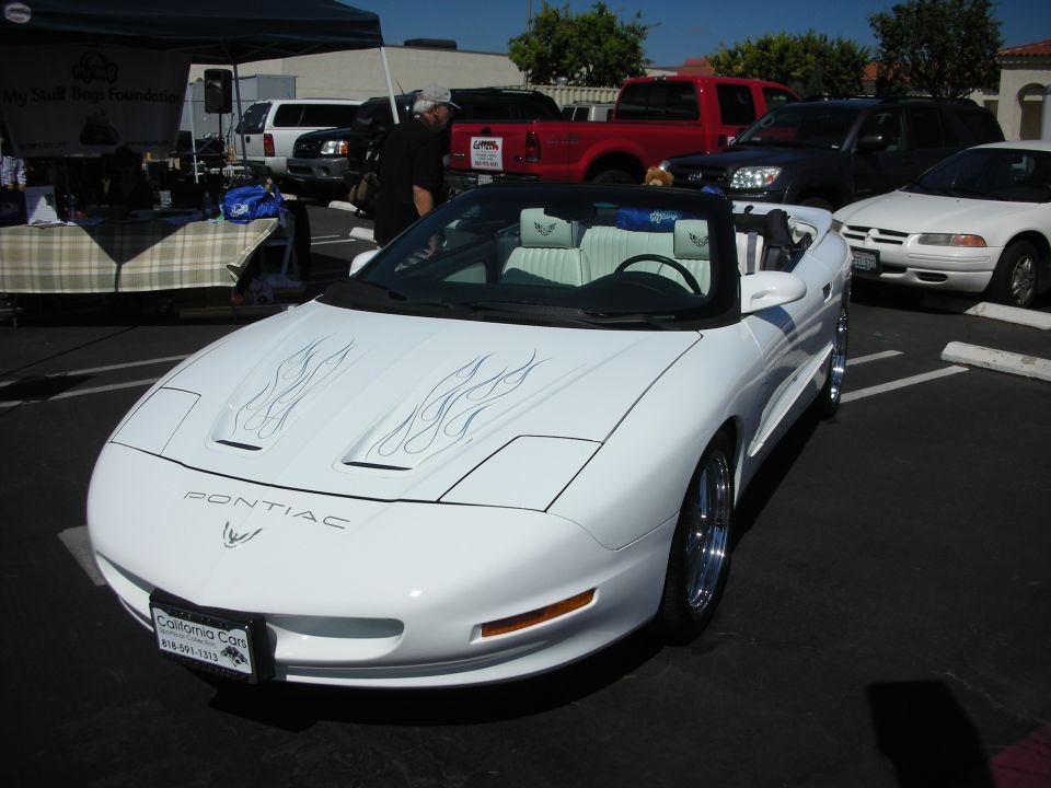 White Pontiac Firebird convertible with flame decals, chrome wheels, and custom interior