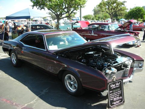 1998 Ford Crown Victoria - A 1967 Buick Riviera is displayed with its hood open at a car show, with other vehicles visible.