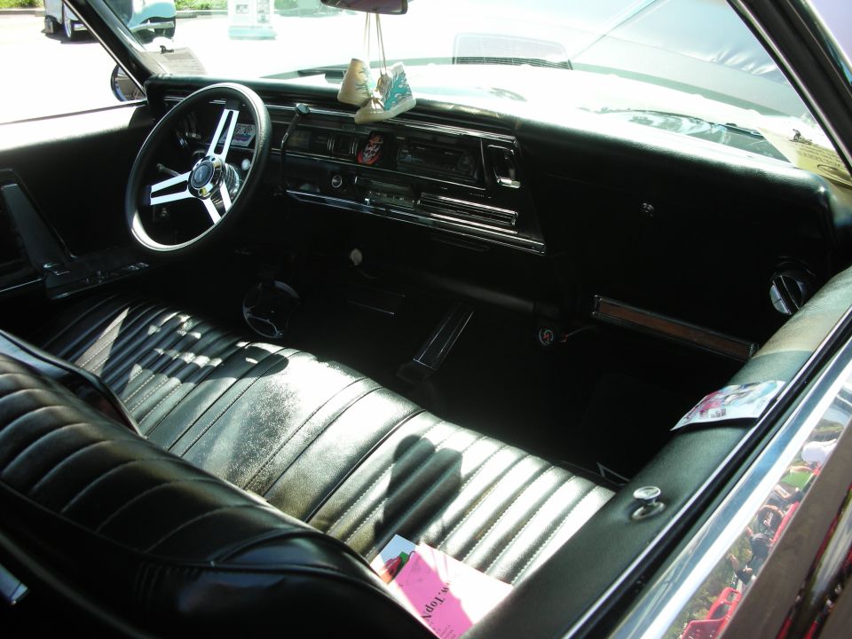 Interior of a classic car with black vinyl seats, a chrome steering wheel, and a dashboard with a radio