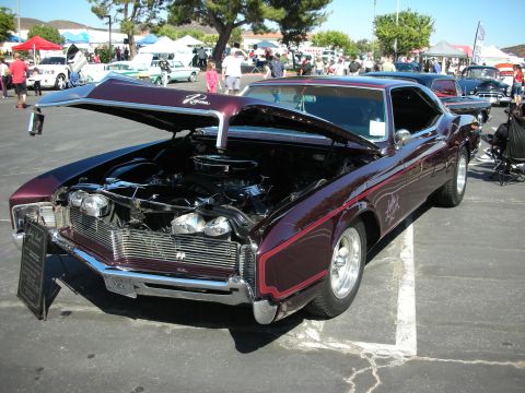 1998 Ford Crown Victoria - A classic car show features a vintage Buick Riviera with its hood raised to display the engine.