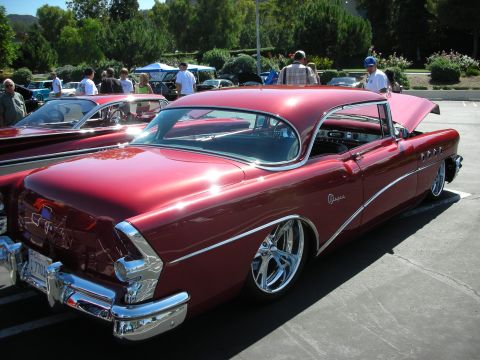 1998 Ford Crown Victoria - A classic red Buick coupe is displayed at a car show, custom wheels and extensive chrome detailing.