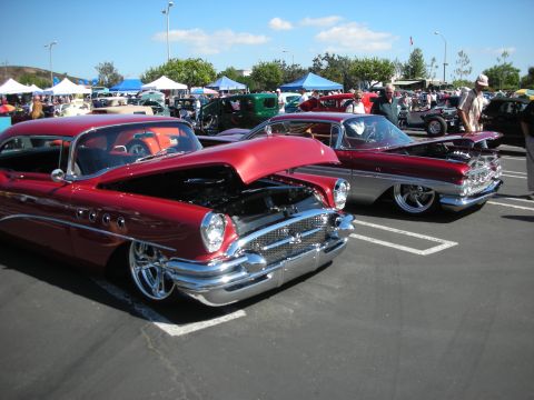 1998 Ford Crown Victoria - Two classic cars are displayed at a car show, both with hoods open, revealing their engines.