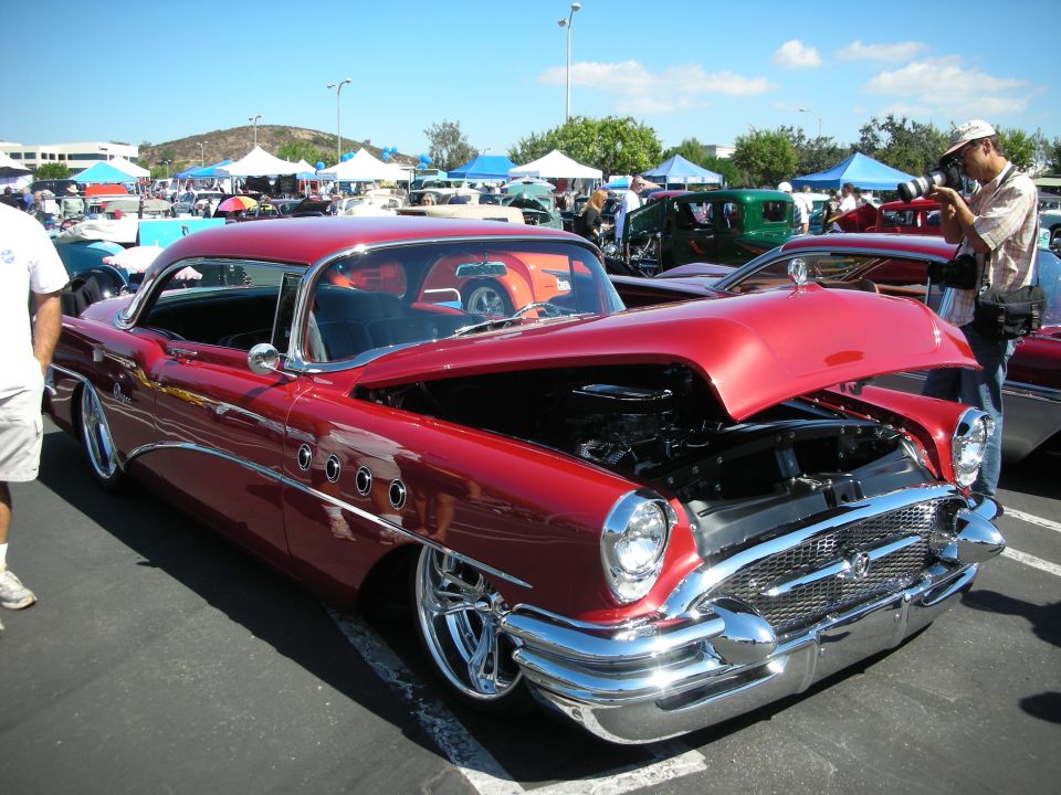 Red 1955 Buick Special two-door hardtop with hood open, showing engine. Parked at car show