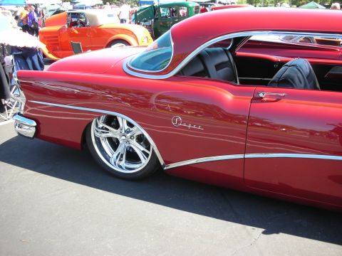 1998 Ford Crown Victoria - A shiny red custom coupe with chrome wheels is parked at an outdoor car show.