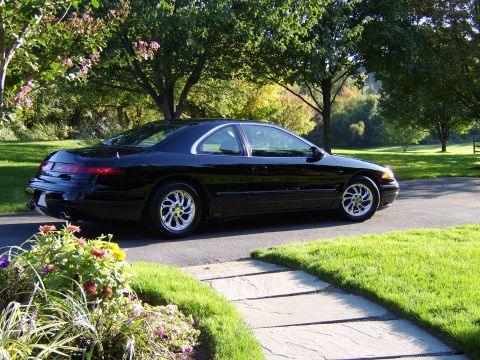 1996 Mercury Grand Marquis - A black coupe is parked on a paved driveway, surrounded by lush green grass and trees.