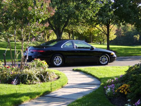 1996 Mercury Grand Marquis - A black coupe is parked on a paved driveway surrounded by lush green grass and trees.