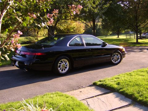 1996 Mercury Grand Marquis - A black coupe is parked on a driveway in front of a grassy yard and trees.