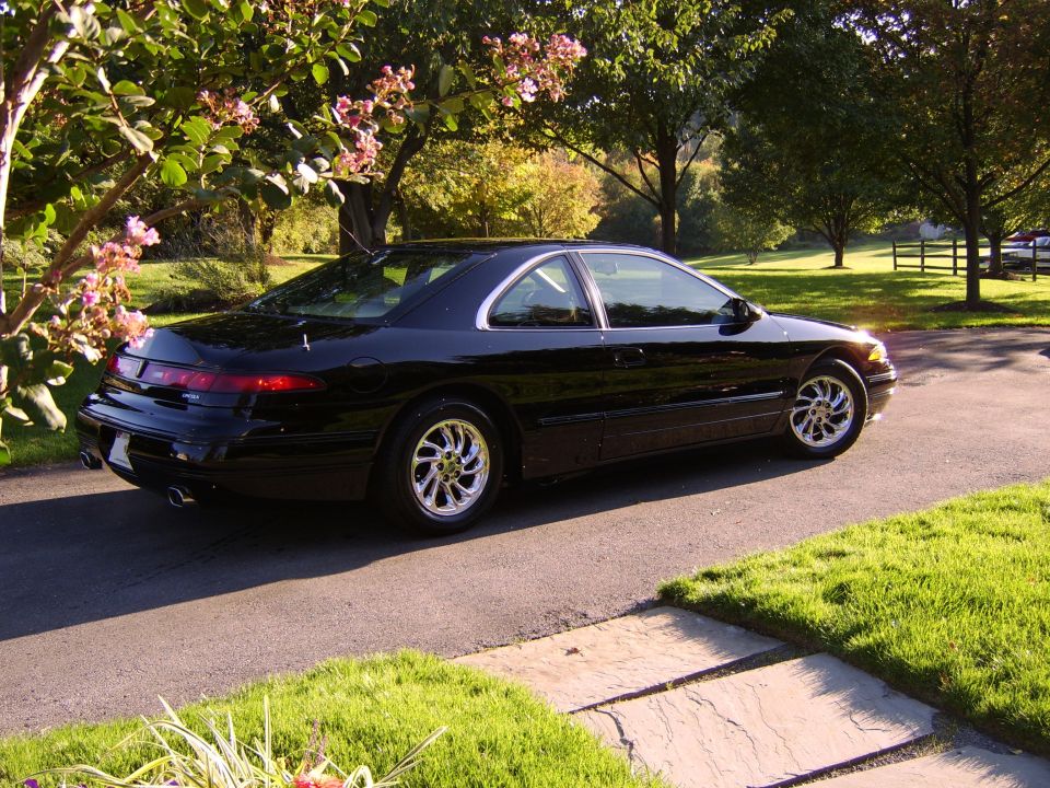 Black coupe rear 3/4 view on driveway with chrome wheels and dual exhaust