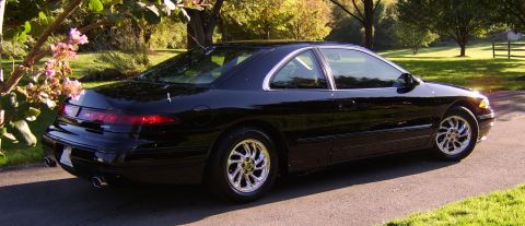 1996 Mercury Grand Marquis - A black coupe with chrome wheels is parked on a driveway surrounded by greenery and trees.