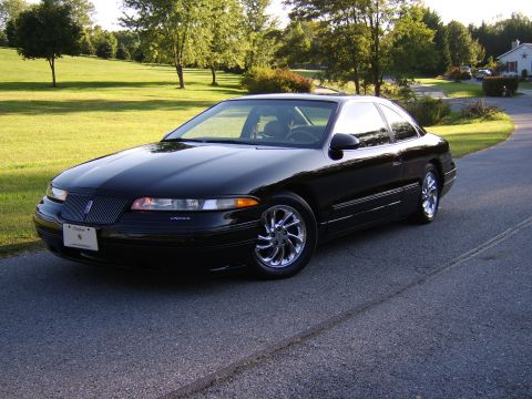 1996 Mercury Grand Marquis - A black Lincoln Mark VIII coupe is parked on a road with a grassy hill and trees in the background.