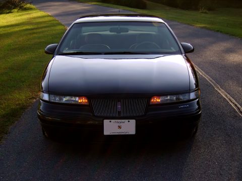 1996 Mercury Grand Marquis - A black Lincoln Mark VIII is shown from the front, parked on a paved road with grass on the side.