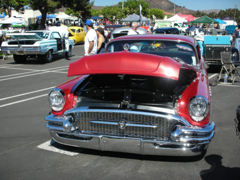 1998 Ford Crown Victoria - A shiny red classic car is displayed with its hood open at an outdoor car show.