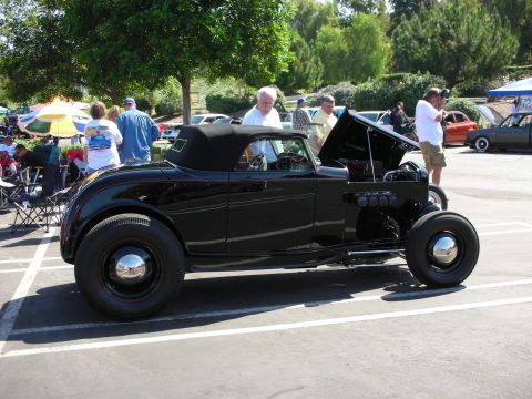 1998 Ford Crown Victoria - Black hot rod convertible at a car show with people around.