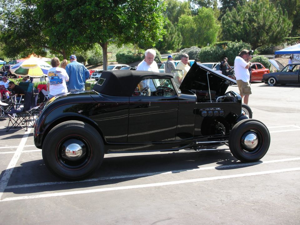 Black convertible hot rod with black top, hood open showing engine. Chrome hubcaps on black wheels