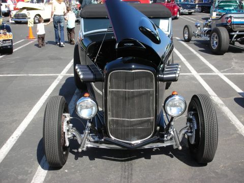 1998 Ford Crown Victoria - A black hot rod is displayed with its hood open at an outdoor car show.