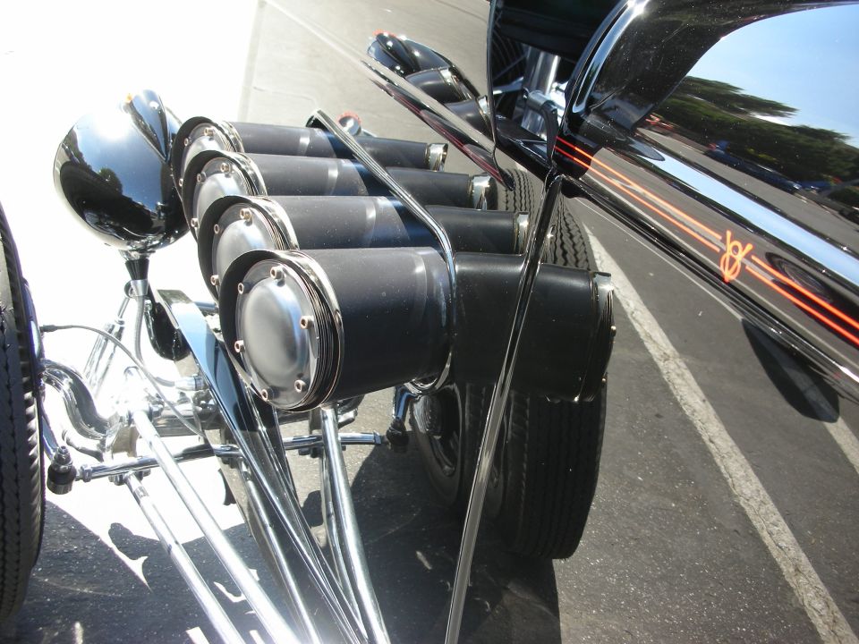 Close-up of a hot rod's stacked exhaust pipes and shiny black body with orange pinstripes