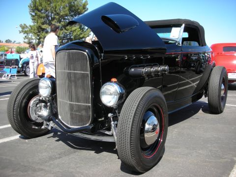 1998 Ford Crown Victoria - A black hot rod is displayed at a car show with its hood open.