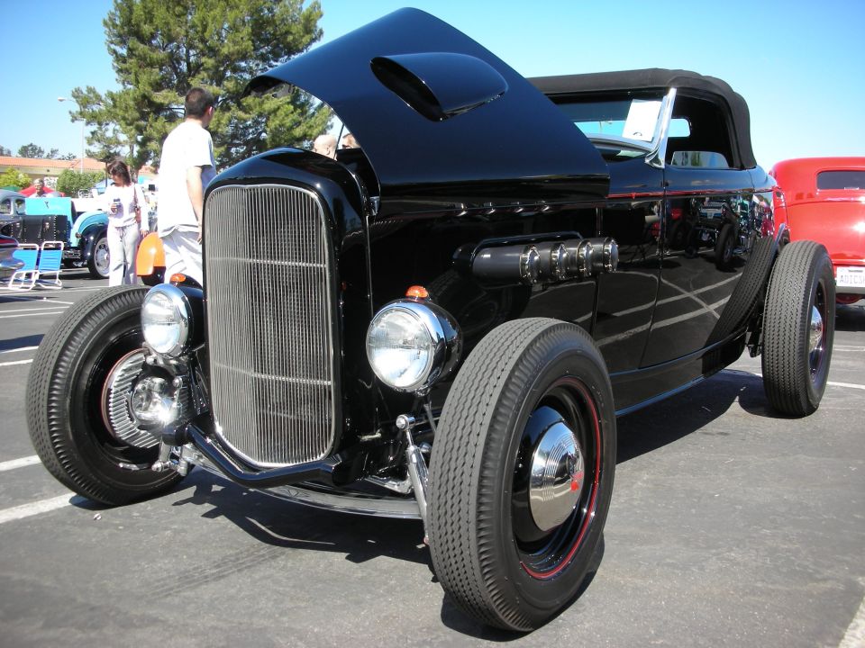 Black hot rod with hood open, chrome grille, and exposed exhaust pipes