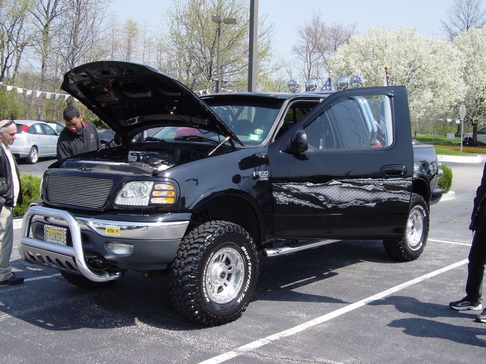 Black Ford F-150 pickup truck with hood and driver door open, aftermarket wheels, and bull bar