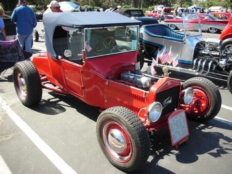 1998 Ford Crown Victoria - A red Ford Model T hot rod is displayed at a car show, parked next to other custom vehicles.