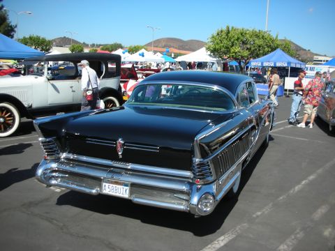 1998 Ford Crown Victoria - Black 1957 Buick sedan at a car show, with other vehicles and tents in the background.
