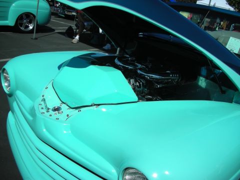 1998 Ford Crown Victoria - A turquoise hot rod is displayed with its hood open, revealing a chrome engine, at an outdoor car show.
