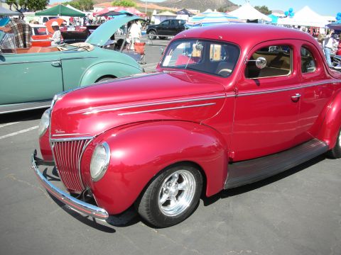 1998 Ford Crown Victoria - A bright red 1939 Ford coupe is parked next to a teal convertible at a car show.