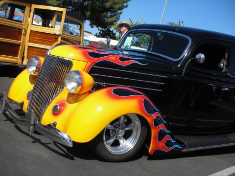 1998 Ford Crown Victoria - A custom hot rod with a flame paint job is parked next to a classic woodie wagon at a car show.