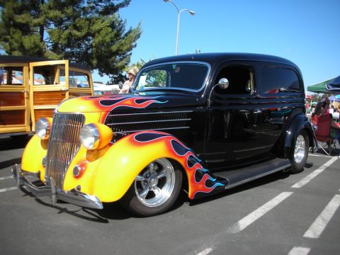 1998 Ford Crown Victoria - A customized hot rod sedan with flame paint is parked next to a wooden station wagon at an outdoor event.