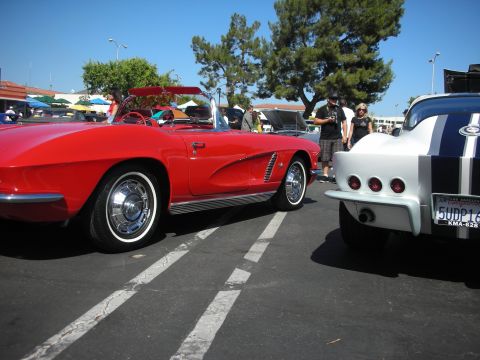 1998 Ford Crown Victoria - A red convertible sports car is parked next to another vehicle with blue racing stripes at a car show.