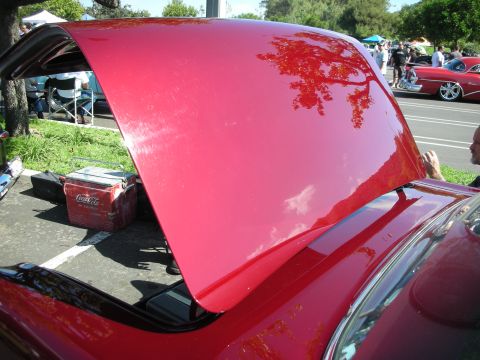 1998 Ford Crown Victoria - Open hood of a red car at a car show, with a vintage Coca-Cola cooler nearby.