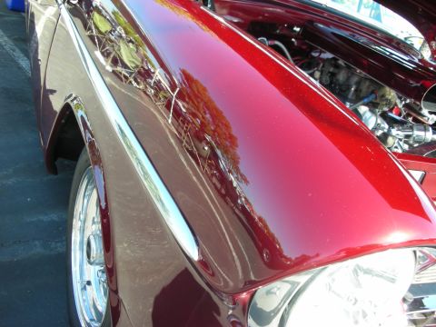 1998 Ford Crown Victoria - A close-up view of a gleaming red classic car's fender and front end, revealing chrome accents and the engine bay.