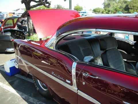 1998 Ford Crown Victoria - A maroon 1956 Chevrolet Bel Air coupe is parked at an outdoor car show with its hood open.