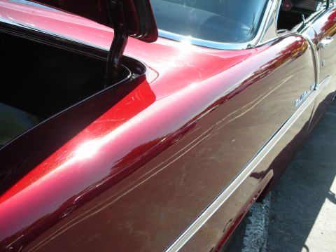 1998 Ford Crown Victoria - Detail of a vintage red car's bodywork, including the open trunk area and a side trim piece.