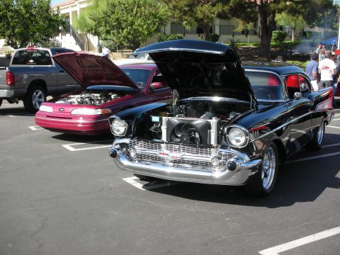 1998 Ford Crown Victoria - Two cars with hoods up at an outdoor car show.