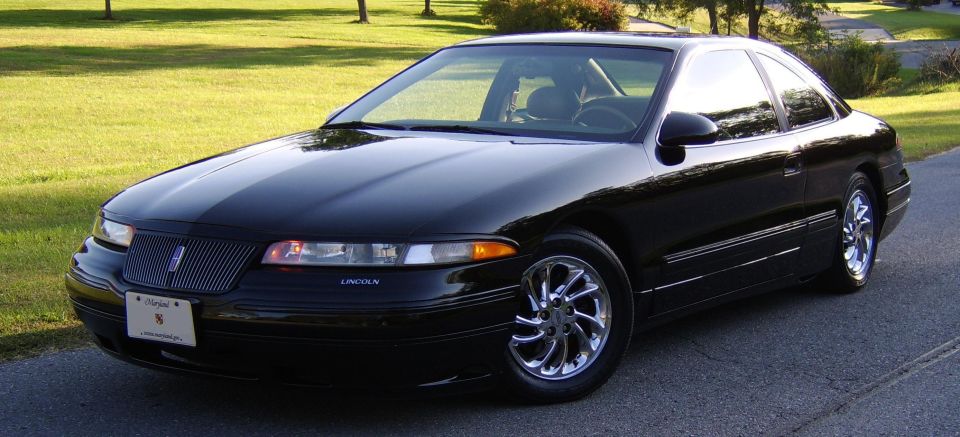 Black Lincoln coupe, front 3/4 view, chrome wheels, parked on road with grass behind