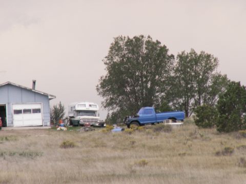 1977 Ford F-250 - A blue pickup truck and a white RV are parked on a grassy area next to a garage.