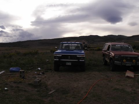 1977 Ford F-250 - Two pickup trucks, one blue and one red, are parked in an open field under a cloudy sky.