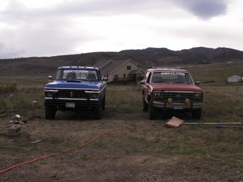 1977 Ford F-250 - Two trucks, a blue 1977 Ford F-250 and a red Ford Bronco, sit in a rural setting under a cloudy sky.