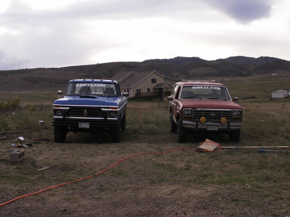 Blue 1977 Ford F-250 and red Ford Bronco parked in a grassy field