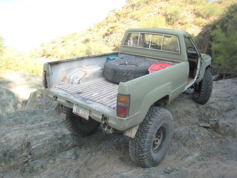 1985 Toyota 4Runner - This olive green pickup truck, likely from the mid-1980s, is equipped for off-road use with large tires and a spare in the bed.