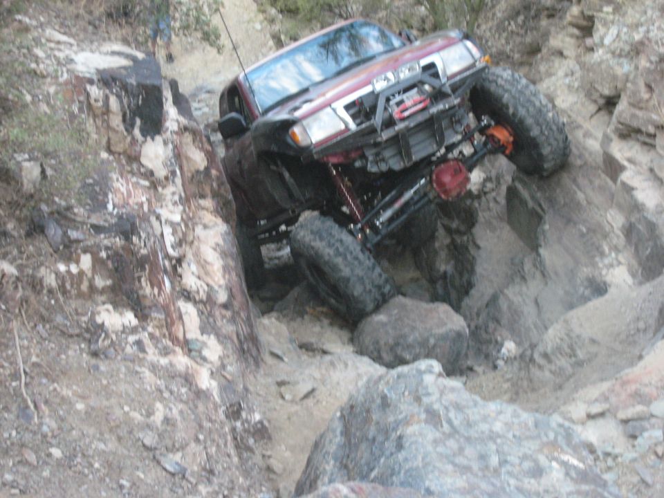 Red SUV with large tires navigating a steep, rocky incline. Visible text: SUPERMOTORS.NET